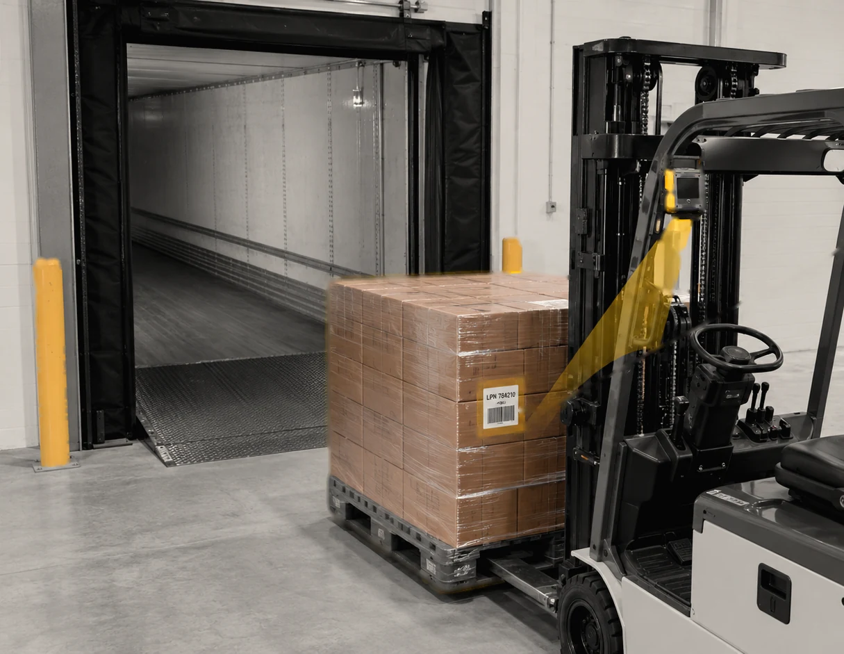 A forklift carries a pallet toward a dock door. The camera on the mast reads the pallet label.